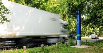 
A truck driving on a federal trunk road drives past a blue Toll Collect enforcement pillar.