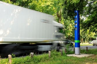 
Ein Lkw fährt auf einer Bundesstraße an einer blauen Kontrollsäule von Toll Collect vorbei.