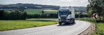 
A semitrailer truck is driving on a federal trunk road through a rural area