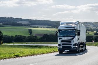 
Een vrachtwagen met oplegger rijdt op een rijksweg door een landelijk gebied