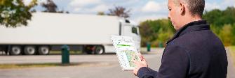 
A driver stands in front of his truck and holds a tablet in his hand; a Toll Collect service partner search is shown on the screen