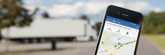 
Der Bildschirm eines Smartphones zeigt die Toll Collect-App. Im Hintergrund parkt ein Lkw.