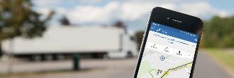 
L’écran d’un smartphone montre l’application Toll Collect. Un poids lourd est garé au second plan.